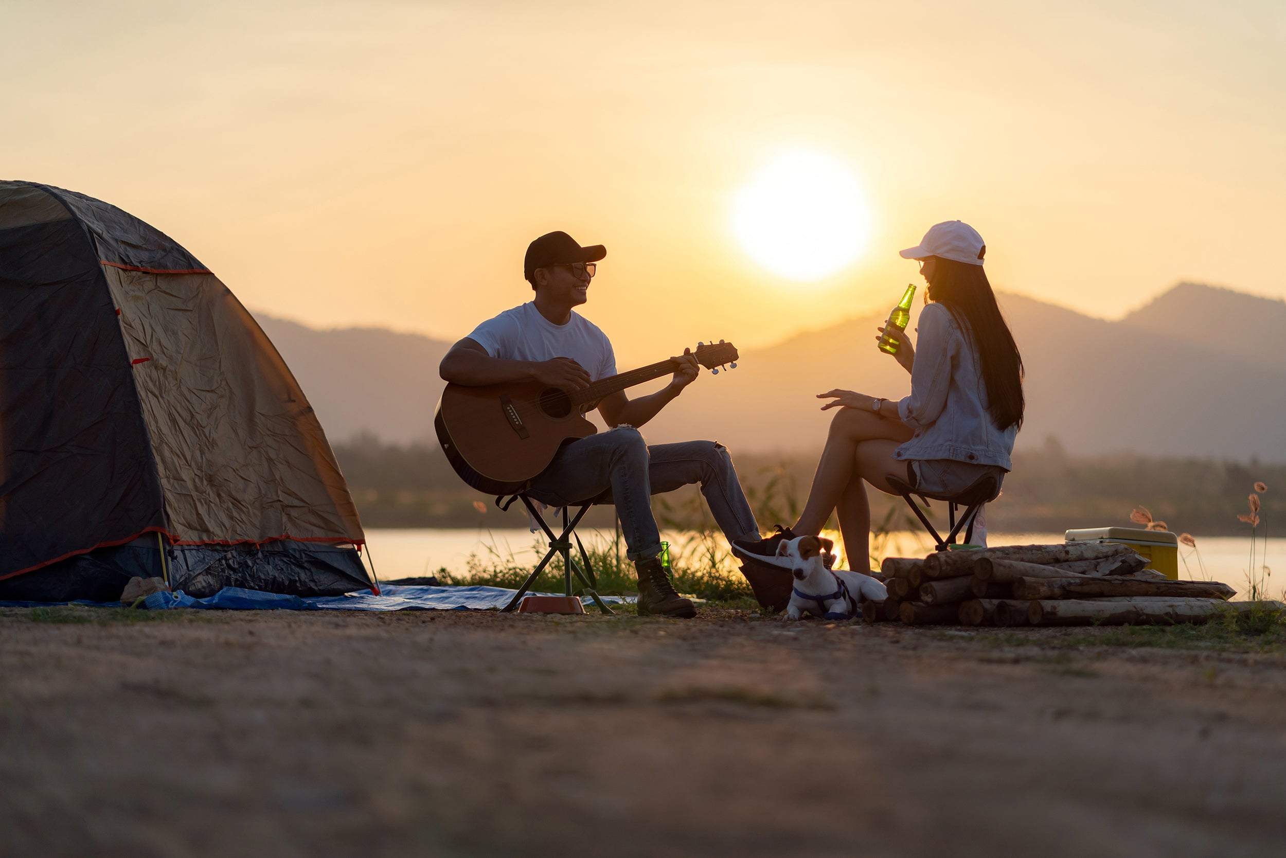 couple sitting by a lake playing guitar with a tent