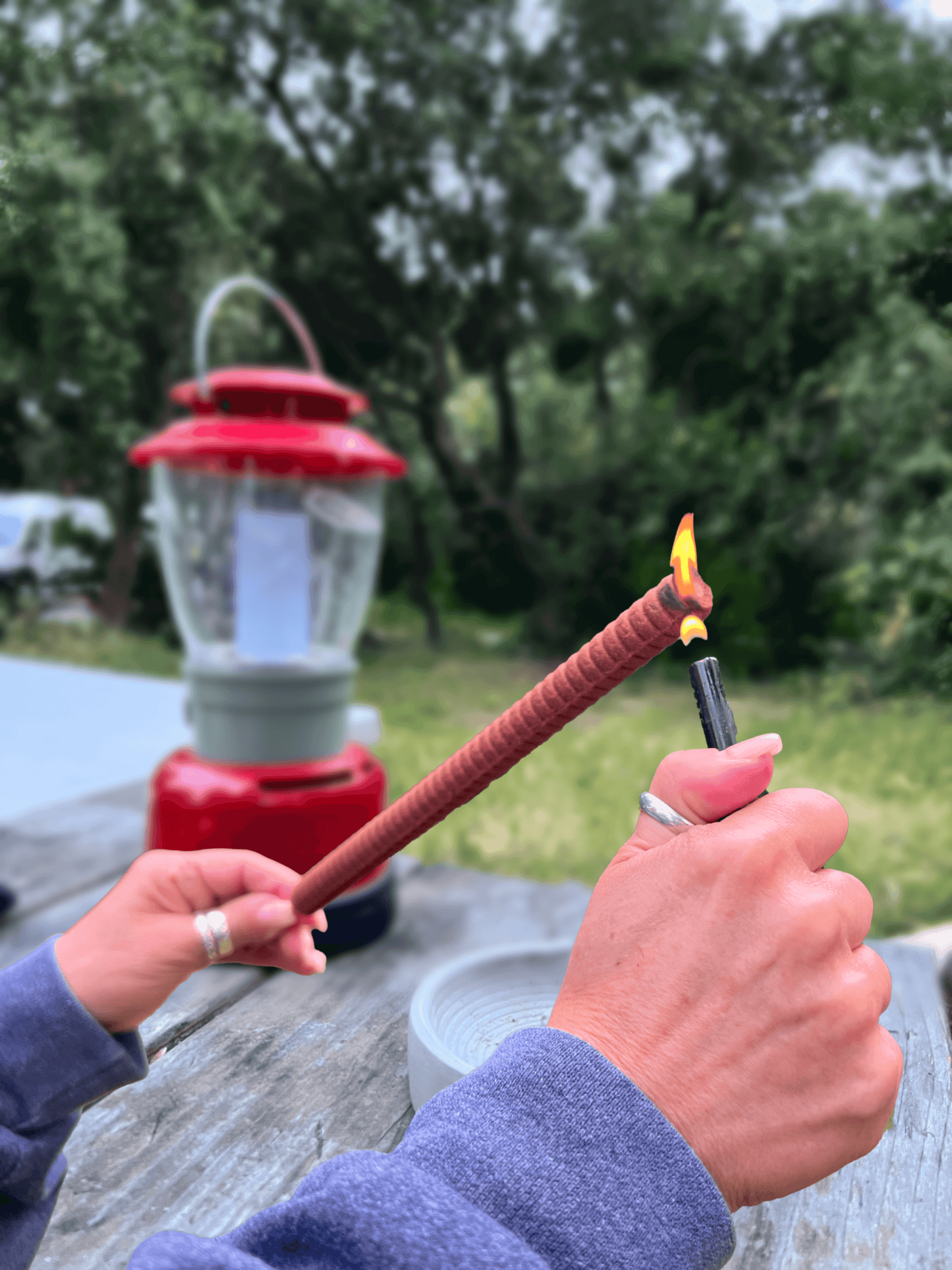 hands lighting a large incense stick with a lighter at a campground