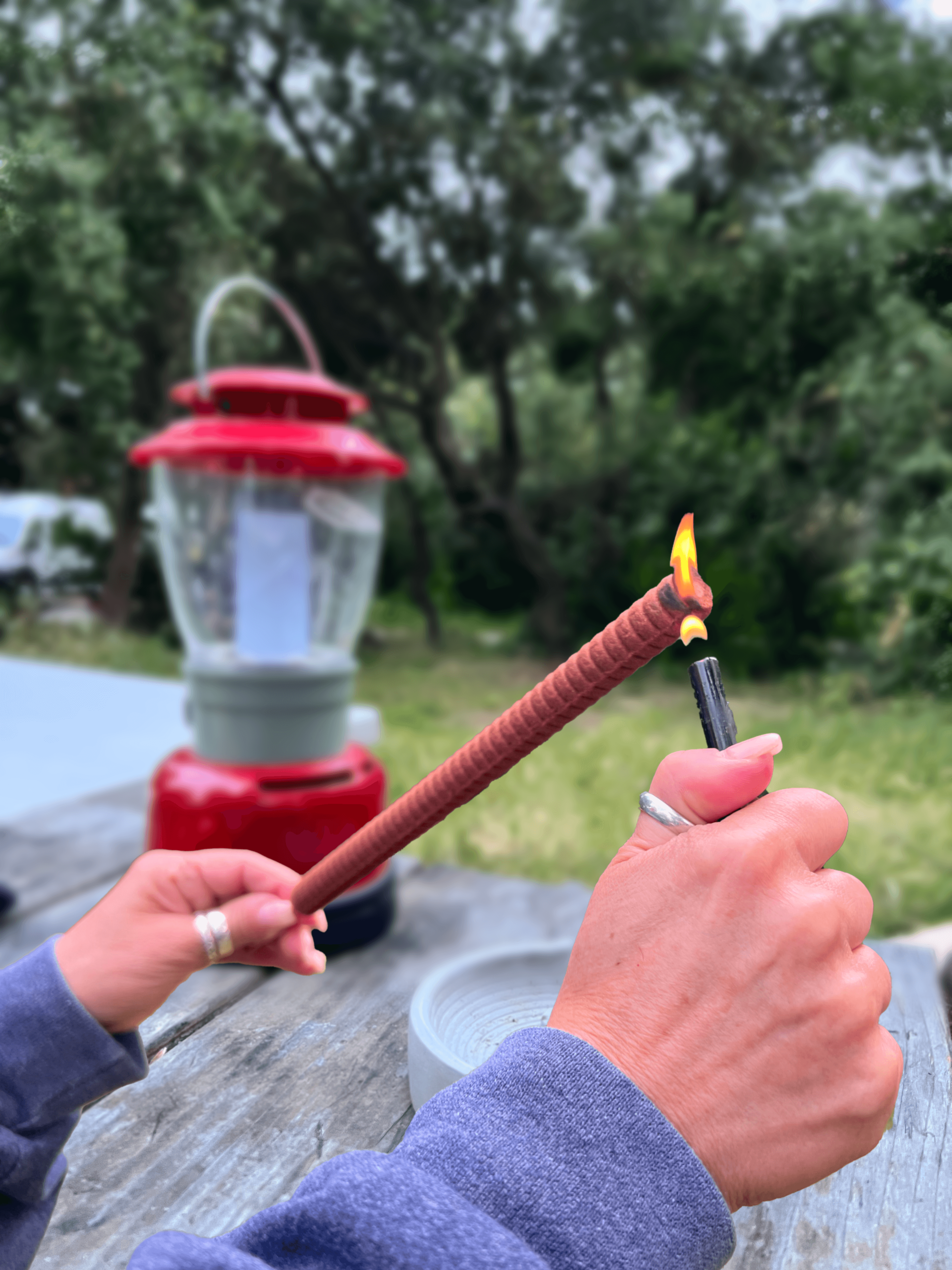 hands lighting a large incense stick with a lighter at a campground